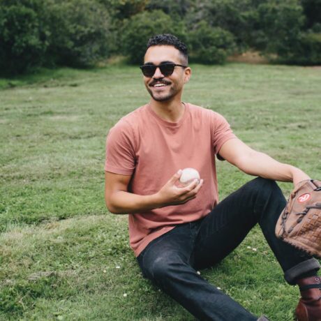 Smiling man sitting in the grass holding a baseball