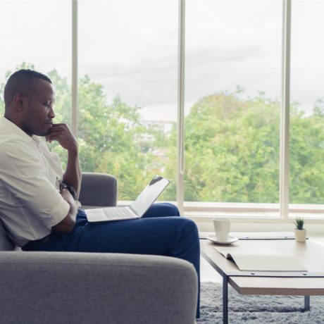 man sitting on a couch and looking at his laptop screen in deep thought