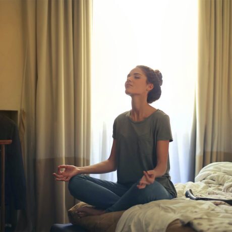 Woman sitting on bed practicing deep breathing to calm anxiety