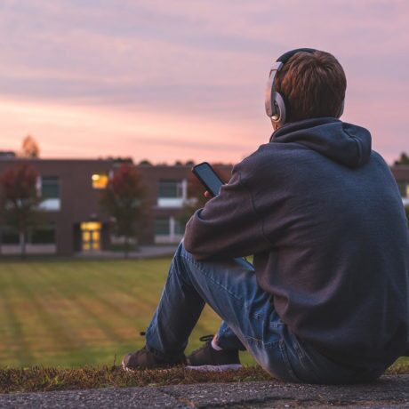 man sitting in an open field with headphones on looking int the distance