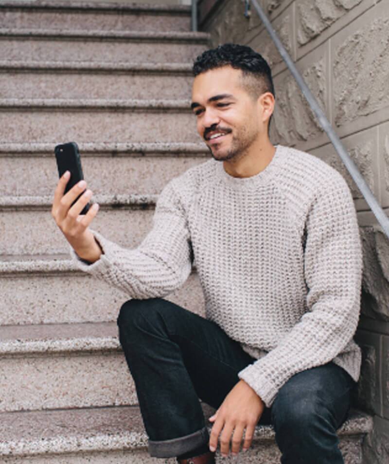 Man sitting on stairs looking at phone and smiling