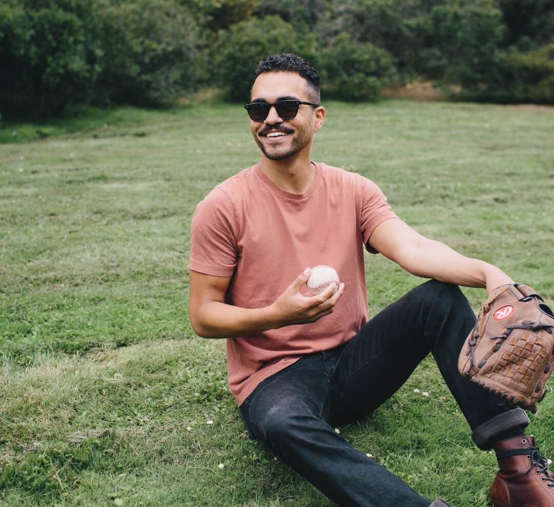 Smiling man sitting in the grass holding a baseball