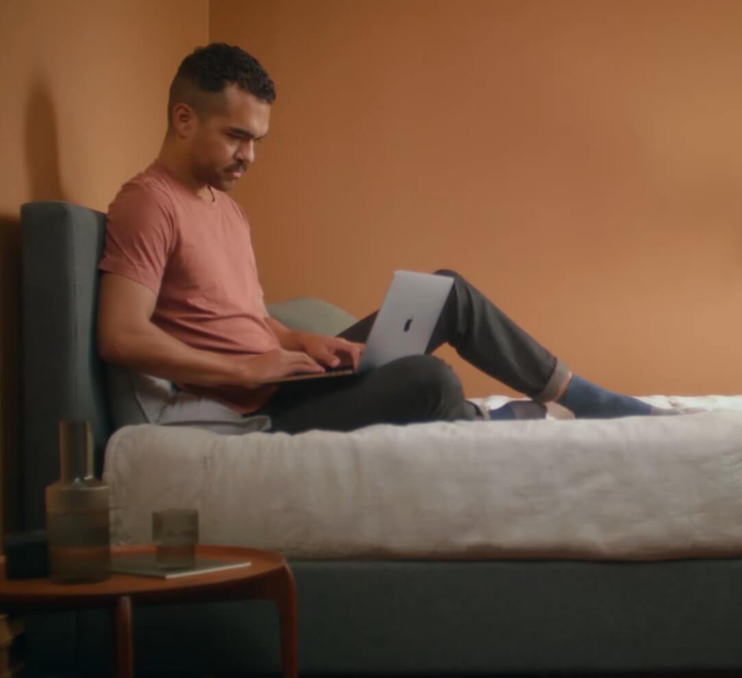 Man sitting on his bed looking at a laptop