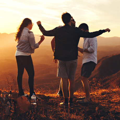 A group of friends standing on the top of a mountain at sunset.
